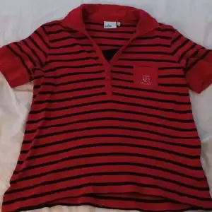 En snygg röd, svart randig tröja med krage och en liten ficka på bröstet med text (3:e bilden)