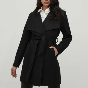 Svart kappa med knytskärp - - Kappa med knytskärp i midjan som är avtagbart. Tryckknappsstängning - Öppna sidofickor - bild tagen från vilas hemsida där modellen är 178 cm lång och bär storlek 38. Aldrig använd 