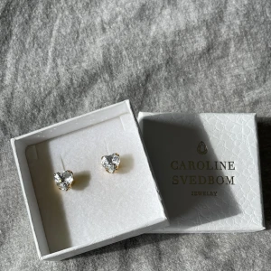 Set från Caroline Svedbom - Örhängen och halsband ur en tidigare limited edition kollektion från Caroline Svedbom. Jättefina och knappt använda. Hjärtformade. Kedjan till halsbandet är 50 cm. Nypris:  Örhängen 495 kr Halsband 595 kr