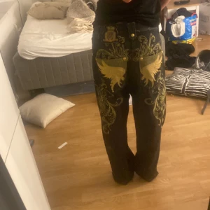 Y2K jeans - Feta jeans med mycket broderade detaljer. Sömmarna är även gul guldiga. Det är samma märke som byxorna på 3 bilden.  Är 167 och dom är bra längd för mig men skulle passa för längre också. Säljer för 400
