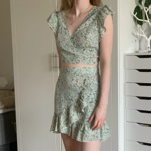 Tvådelad kjol & topp - Tryck gärna på ”köp nu” för billig o spårbar 🥰 Nyskick! Blommigt set med kjol och omlott-topp. Kjolen har en dragkedja vid sidan och toppen knyts lite hur man vill. Materialet är tunt och luftigt, perfekt till sommaren. Säljer endast delarna tillsammans 💗