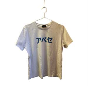 T-shirt med texten APC på japanska. strl L men motsvarar snarare M.  Liten fläck, knappt synlig, se sista bilden. Går säkert bort med fläckborttagning.