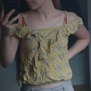 Gul tröja med volanger - En gul tröja med blommor och volanger på armarna och diagonalt över tröjan. Den har även en väldogt strechig midja så den passar många olika storlekar. Den har användts en del men är i mycket bra skick utan några synliga fläckar.