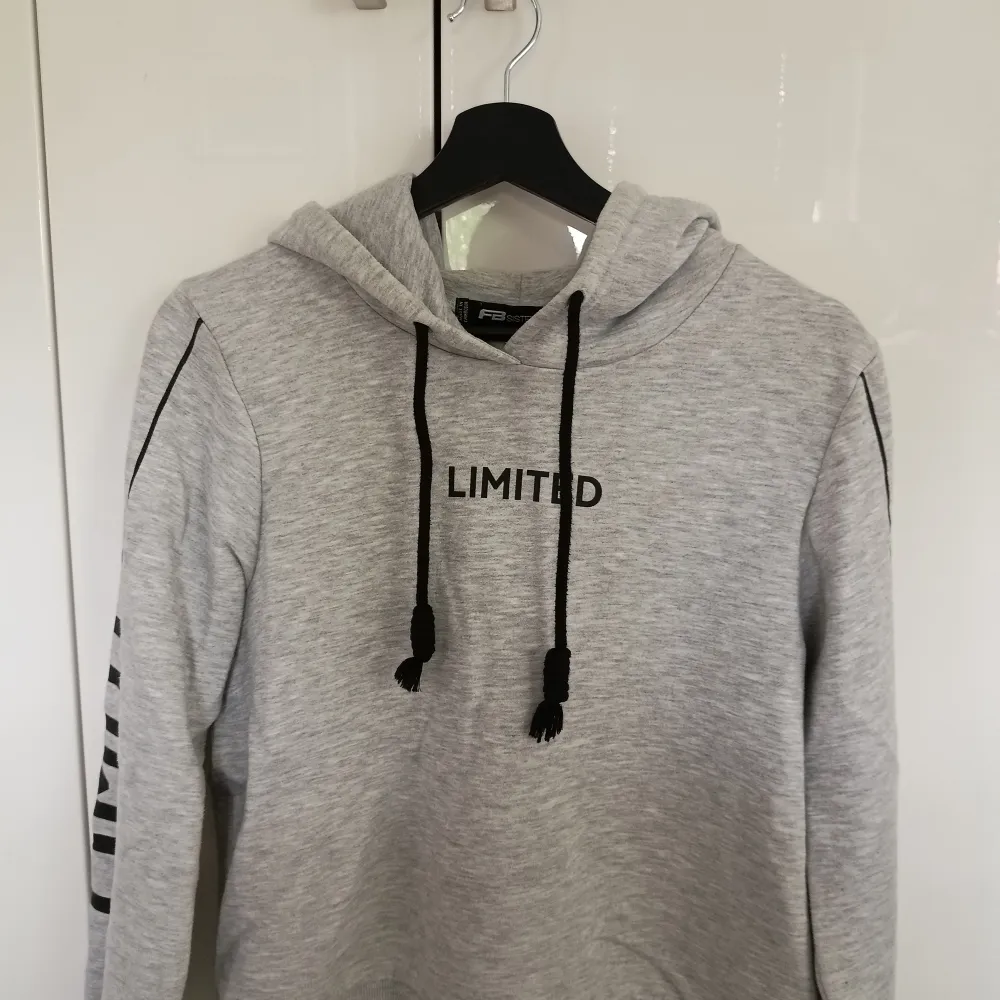 En grå hoodie med svart text och svarta snören. Texten 