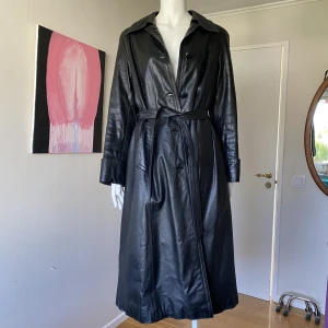 Trenchcoat i läder - Använd ett antal gånger men numera för liten. Den är ganska liten i storleken. Kappans mått i cm: L 118, axelbredd 43, armlängd 57. 