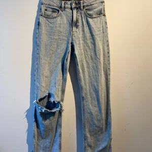 Blåa jeans med hål - Blåa jeans som är lågmidjade, detaljer på fickan bak och nere vid benen, 1 hål i knäet