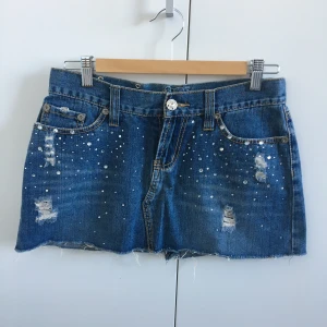 Jeanskjol från River Island - Min syrras gamla jeanskjol från River Island i y2k-stil, jättefint skick! Med dekorativa slitningar och rhinestones. Några få stenar (typ 3 st) saknas men inget allvarligt. Storlek 36, mått: midja 38,3 cm, längd fram 27,8 cm, längd bak 29,8 cm.