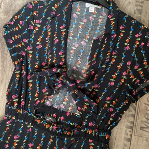 Blommig klänning med knytning fram - Svart blommigt mönstrad klänning med en knytning fram och resår i midjan.