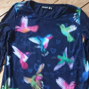Desigual svart tröja med flerfärgat tryck av kolobri fåglar. Extra mesh-lager på framsidan.  Nyskick 