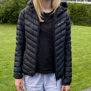 Peak performance dunjacka  - Peak performance höst/vinterjacka i svart med luva och sidfickor. Använd men i bra skick förutom att det finns ett litet hål på högerarmen som har försökts lagas. 
