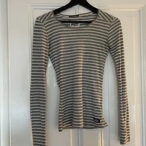 Grå vit randig lång tröja  - Säljer min fina långsemester t-shirt från märket superdry. Den är i storlek xs men skulle säga att den funkar som S också. Säljer för att jag behöver pengar 