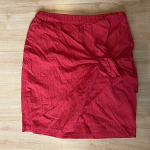 Kort kjol - En kort kjol ifrån Andrea Hedenstedts kollektion med NAKD. Aldrig använd men prislappen borta. Knytdetalj på sidan av kjolen. Inte lika röd i verkligheten som den är på bilden, svårt att få rättvis färg på bild.