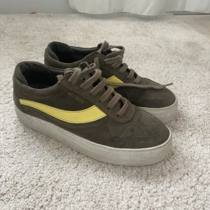 Arigato skor  - Ett par gröna Atigato skor med gula detaljer. Gammal modell, använda men ändå fint skick. Storlek 37. Kontakta vid pris diskuterande