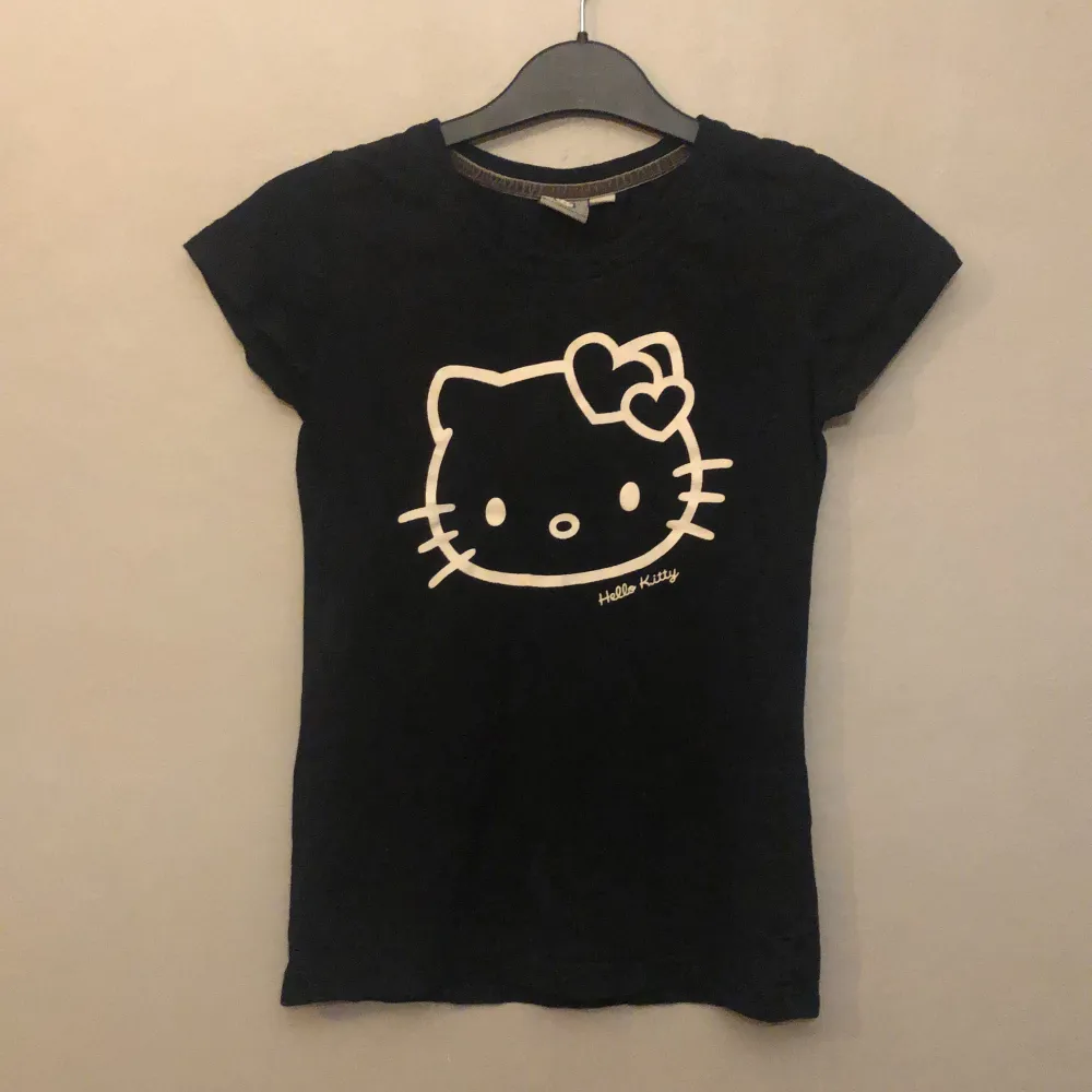 En svart t-shirt med Hello Kitty på ifrån Kappahl💕 Inga defekter vad jag kan se. Jag som är en liten S kan få på mig den, men den är tajt i armhålorna!. T-shirts.