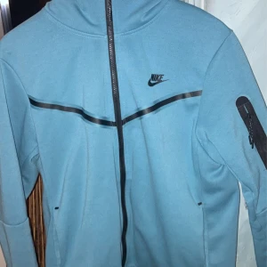 Nike Tech tröja - En ljusblå Nike Tech tröja men en lite skada som är enkel och fixa annars är resten av tröjan som ny🤩