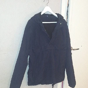 Medelvarm mörkblå jacka 40/42 divided - Medelvarm jacka utan dragkedja som man bara drar på över huvudet. Mjukt innerfoder. Stor ficka på mitten av framsidan av jackan. Divided. Strl 40/42. Helt okej skick. Mörkblå. Bomull och polyester. 