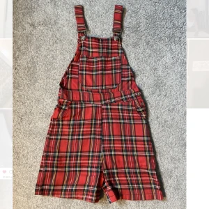 Rutiga hängselbyxor  - Gothinc röda hängselbyxor som passar perfekt på en randig tröja och nätstrumpbyxor. Det sticker ut lite trådar på ett ställe men annars är skicket bra