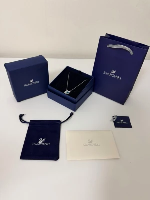 Blå swarovski halsband - Elegant halsband från Swarovski med ett silverfärgat kedja och ett hänge i form av en svan dekorerad med blå och vita kristaller. Kommer med original ask, påse och certifikat. Perfekt för dig som gillar gnistrande detaljer och exklusiv design.