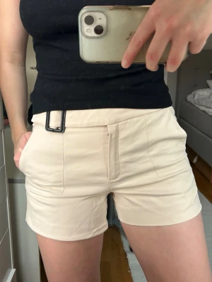 Beige shorts med bälte och fickor - Snygga beige shorts med ett brett bälte och svart spänne. Shortsens design är stilren med två framfickor och diskreta sömdetaljer. Midwaist. 