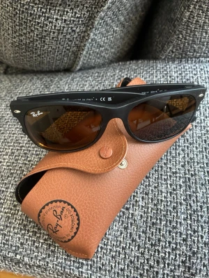 Svarta Ray-Ban Wayfarer solglasögon - Säljer ett par original Ray-Ban New Wayfarer (RB2132) i nyskick. Glasögonen är oanvända och kommer med original Ray-Ban-fodral.  New Wayfarer är en av Ray-Bans mest populära modeller med en tidlös design som passar både till vardag och sommarens alla aktiviteter.  📌 Modell: Ray-Ban RB2132 New Wayfarer 📌 Färgkod: 622/17 (svart båge med bruna glas) 📌 Storlek: 55-18 📌 Skalmlängd: 145 mm  ⚠️ Viktigt: Glasögonen har slipade styrkeglas monterade. Köparen behöver därför själv byta glas efter egen synsty