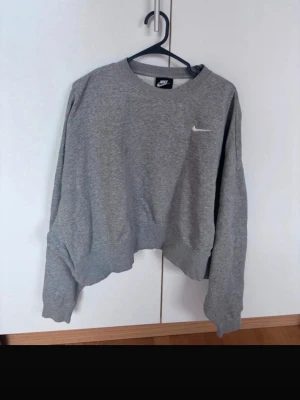 Grå sweatshirt från Nike - En klassisk grå sweatshirt från Nike med rund halsringning och diskret vit logga på bröstet. Tröjan har en avslappnad passform och långa ärmar. Perfekt för en sportig och casual stil.