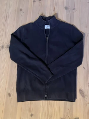 Navy Bläck Fullziptröja - Mjuk och enkel navy full zip tröja med hög krage och hel dragkedja framtill. Perfekt för lager på lager och har en stilren look utan synliga loggor eller detaljer. Långärmad och i ett skönt material som håller värmen.
