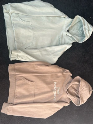 Beige Peak Performance hoodie - Säljer en beige hoodie från Peak Performance med broderad logga på bröstet. Hoodien har en klassisk känguruficka och mjukt material på insidan. Perfekt för dig som gillar en clean och avslappnad stil.