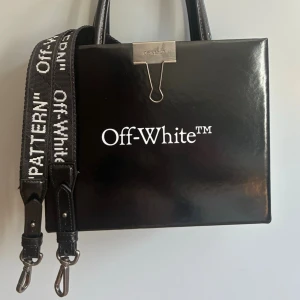  Off-White ”SCULPTURE” clip pattern Virgil 2013 Bag - Snygg svart handväska från Off-White. Nypris ca 1000€  med vit logotyp på framsidan och textdetaljer på baksidan. 2013 virgil for offwhite sculpture  collection, väska i lack med lång avtagbar rem och metalldetaljer, inga repor eller skador. Köptes på versitaire collective 2024 använt den 3-4 gånger. Kommer med dustbag. Väskan har en fyrkantig form, dubbla handtag och en bred axelrem med Off-White och 'PATTERN' tryckt i vitt. Materialet är glansigt och ger en lyxig känsla.
