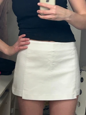 Vit kjol med shorts  - Säljer en stilren vit shortskjol i bomull med enkel design och raka linjer. Kjolen har hög midja och diskreta fickor baktill