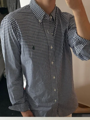 Rutig skjorta från Ralph Lauren - Klassisk långärmad skjorta från Ralph Lauren i blåvitt rutigt mönster. Skjortan har button-down krage, vita knappar framtill och en liten grön broderad logga på bröstet. Tillverkad i mjuk bomull och har en normal passform. Lite missfärgad i kragen annars bra skick 