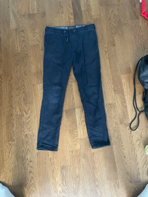 Mörkblå chinos med dragsko - Snygga mörkblå chinos med smal passform och dragsko i midjan. Byxorna har sidofickor fram och två passpoalfickor bak. Perfekta för en avslappnad men ändå stilren look. Materialet känns mjukt och bekvämt. Helt nya är värda ca 1300kr