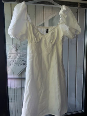 Vit kort klänning med puffärm - Superfin vit klänning från H&M med puffiga korta ärmar och tyg formad över bröstet. Klänningen har en söt v-ringning och är tillverkad i ett lätt tyg som känns luftigt. Perfekt för varma dagar och ger en snygg touch 