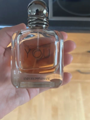 Emporio Armani Stronger With You parfym - Emporio Armani Stronger With You är en elegant parfym i en genomskinlig glasflaska med rundade kanter och silverfärgad kork. Doften har en varm, bärnstensfärgad vätska och flaskan har en stilren design med märkets logga på framsidan.