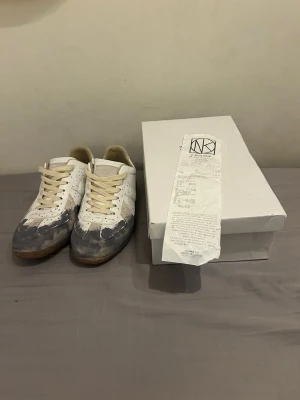 Maison Margiela GAT sneakers vita/grå - Maison Margiela GAT sneakers i vitt och grått med beige skosnören och gummisula. Klassisk låg modell med distinkt färgblock och retrovibbar. Levereras med originalkartong och kvitto. Lite slinta på utsidan. 