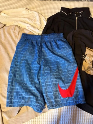 Paket med kläder  - I detta paket finns det blåa Nike badbyxor i storlek S.  En svart calvinekline tröja i storlek 164/14år. Två T-shirts/skjortor med halvdragkedja i storlek xs. Och en vit t shirt i storlek xs