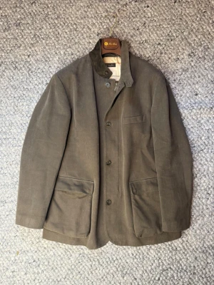 loro piana roadster jacka - Stilren olivgrön jacka från Loro Piana  med tre knappar framtill och stora utanpåfickor. Jackan har en klassisk krage som kan bäras både uppfälld och nedvikt samt ett rutigt innerfoder. Tillverkad i ett mjukt tyg som ger en avslappnad men ändå dressad look.