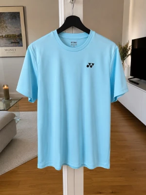 Ljusblå Yonex t-shirt i polyester -  ljusblå t-shirt från Yonex som passar perfekt för sportiga aktiviteter eller varma dagar och en fräsch outfit .