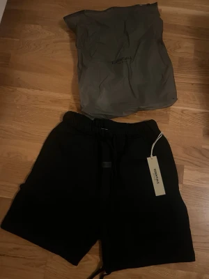 Svarta shorts från Essentials - Svarta shorts från Essentials med elastisk midja och snörning. Klassisk loose fit och diskret logga framtill. Perfekta för en avslappnad stil och tillverkade i mjukt material för extra komfort.