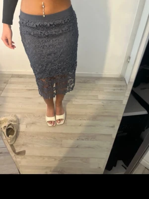 Mörkblå spetskjol med blommönster - Säljer en mörkblå, midilång kjol i spets med blommigt mönster. Kjolen har elastisk midja och transparent nederdel som ger en snygg och trendig look. Perfekt att styla med crop top eller stickad tröja.