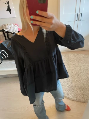 Svart blus från Black Story - Svart, luftig blus från Black Story i storlek S (36/38). Blusen har v-ringning, långa ärmar och ett avslappnat fall med volangdetaljer. Tillverkad i ett mjukt, tunt tyg som känns skönt mot huden. Perfekt att styla med jeans eller kjol.
