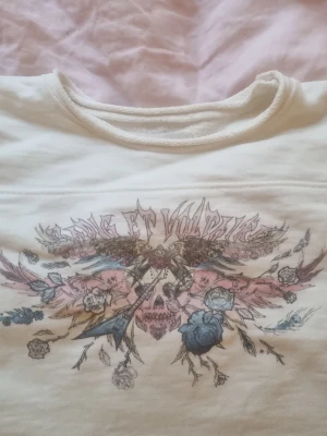 Vit långärmad topp från Zadig & Voltaire - Vit långärmad topp från Zadig & Voltaire med ett stort tryck framtill i pastellfärger. Trycket har motiv av blommor, fåglar och en dödskalle, samt texten 'Zadig et Voltaire' upptill. Rund halsringning och mjukt material. Den har små fläckar som jag ringat in. Säljer pga den är för liten 