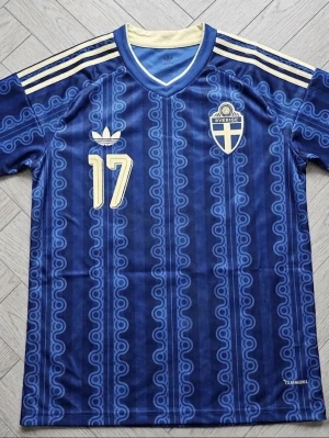 Blå Sverige fotbollströja Adidas - Säljer en blå fotbollströja från Adidas med Sveriges landslagsemblem och nummer 17. Tröjan har gula detaljer, klassiska Adidas-ränder på axlarna och namnet Gyökeres på ryggen. Tillverkad i lätt och ventilerande material, perfekt för träning eller match.