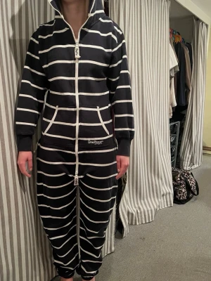 Svartvit randig OnePiece jumpsuit - Super mysig one piece som köptes ny 899kr. Mysig svart jumpsuit från OnePiece med vita horisontella ränder, dragkedja hela vägen, huva och fickor framtill. Perfekt för chill hemma. Tjockt och mjukt material som känns skönt mot huden.