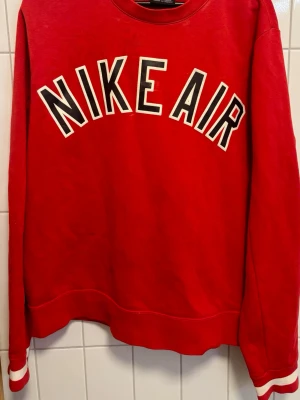 Nike Air sweatshirt - Röd sweatshirt från Nike Air med stor vit och svart logga framtill. Tröjan har rund halsringning, långa ärmar och vita detaljer vid ärmsluten. Perfekt för en sportig och avslappnad stil. Passar stlk S/M.