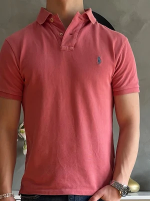 Ralph Lauren pikétröja i rosa och storlek S - Snygg och stilren Ralph Lauren pikétröja i storlek S perfekt för sena sommarnätter eller fina middagar. Tröjan är knappt använd i minimalt slitage förutom att ättiksyran har låsnat då den hängt i den. Priset går att diskutera och jag skickar fort.