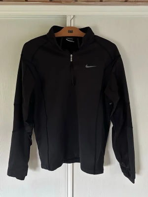 Svart Nike Golf Dri-Fit tröja - Svart långärmad träningströja från Nike Golf med halv dragkedja och Dri-Fit-material som andas. Tröjan har en stilren design med Nike-logga på bröstet och är perfekt för sportiga aktiviteter. Storlek M men sitter mer som S. Säljes då den inte passar. Väldigt bra skick! 