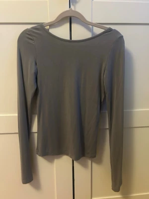 Grå långärmad topp med djup rygg - Snygg grå långärmad topp med tight passform och djup, rundad rygg. Tillverkad i ett mjukt och stretchigt material som sitter skönt på kroppen. Perfekt för att skapa en stilren och enkel look. Storlek xs fårn bikbok men har klippt av lappen i ryggen. Pris kan diskuteras 💕 säljer då den tyvärr bara kommit till användning max 5 gånger
