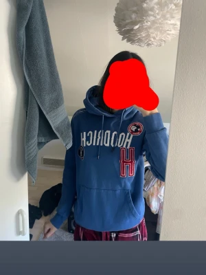 Blå hoodie från Hoodrich med tryck - Säljer en blå hoodie från Hoodrich med stora vita och röda tryck framtill, inklusive ett stort H och flera patches. Hoodien har huva med dragsko och en stor magficka. Perfekt för dig som gillar streetwear och vill sticka ut lite extra. Orginal priset är 800kr o säljer för 550kr 