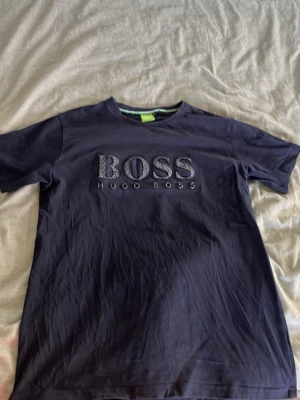 Svart t-shirt från Hugo Boss - Svart t-shirt från Hugo Boss med stort BOSS-tryck på bröstet. Klassisk rund halsringning och korta ärmar. Tillverkad i mjuk bomull som känns skön mot huden. Perfekt för en stilren och avslappnad look.