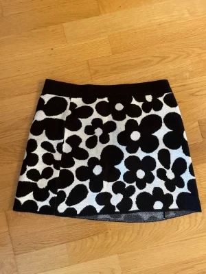Blommig svartvit kjol från H&M Divided - Supersnygg kort kjol från H&M Divided med stora blommor i svart och vitt. Kjolen har en rak passform och är stickad i mjukt material, perfekt för att lyfta vilken outfit som helst.